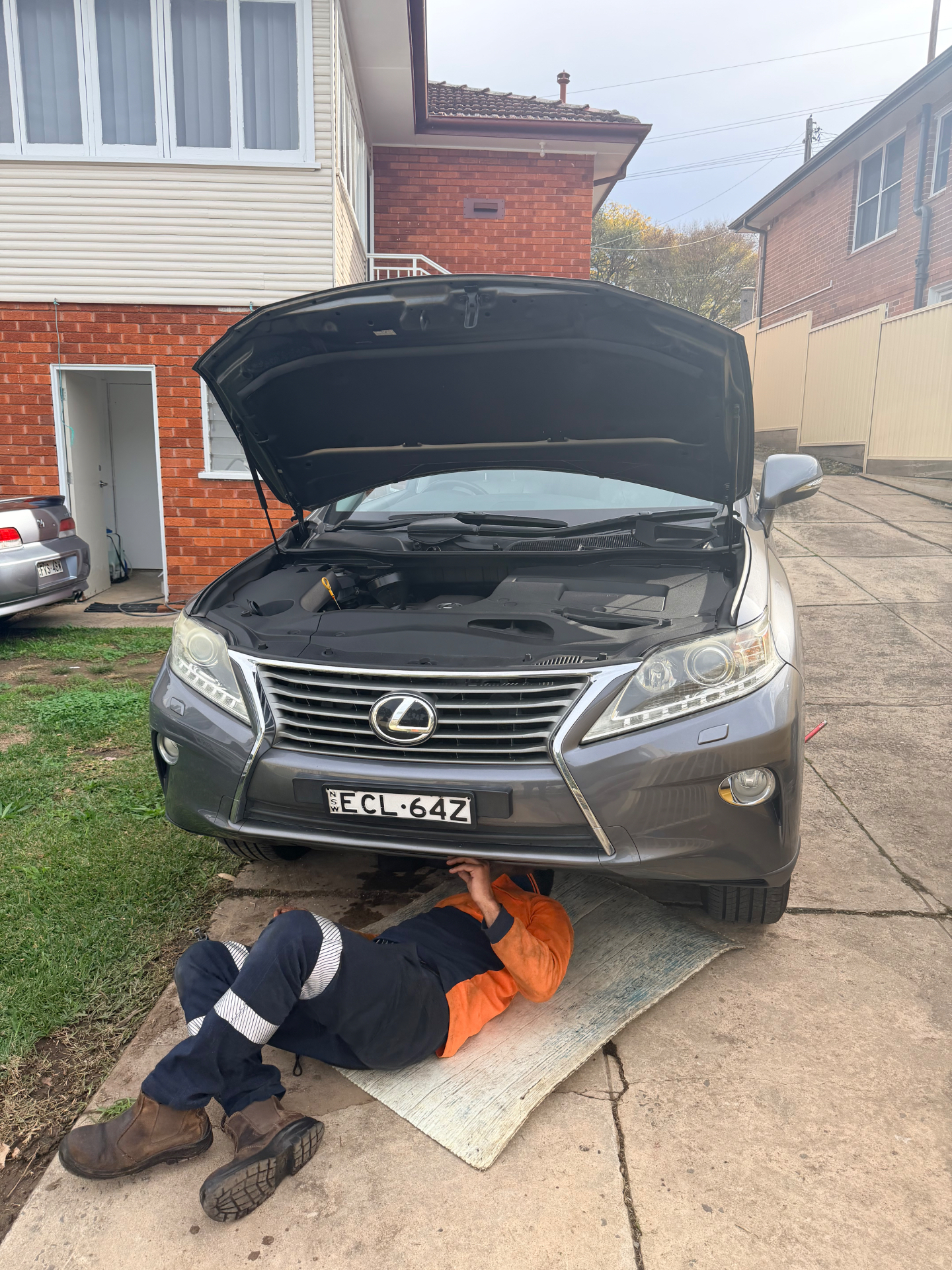 Mobile mechanic working underneath a Lexus RX on a residential driveway