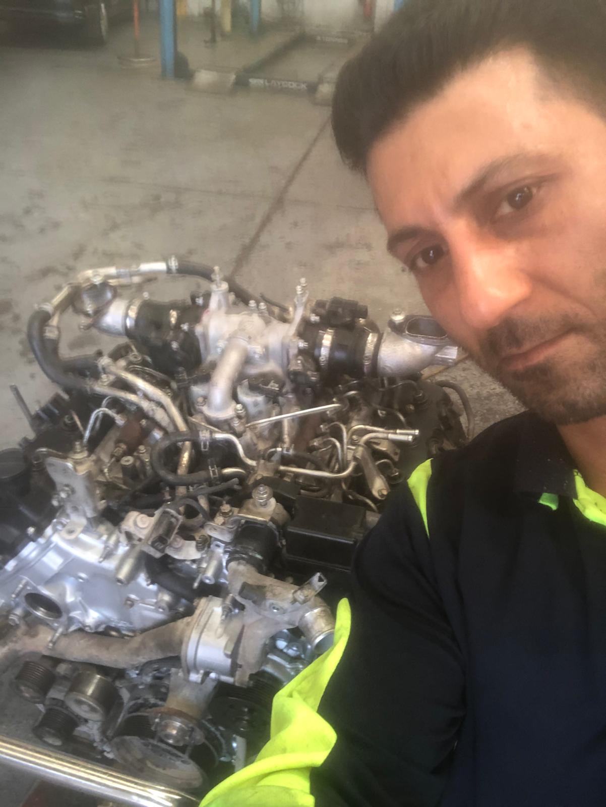 Mehdi next to a stripped engine block with turbo and injectors during a rebuild
